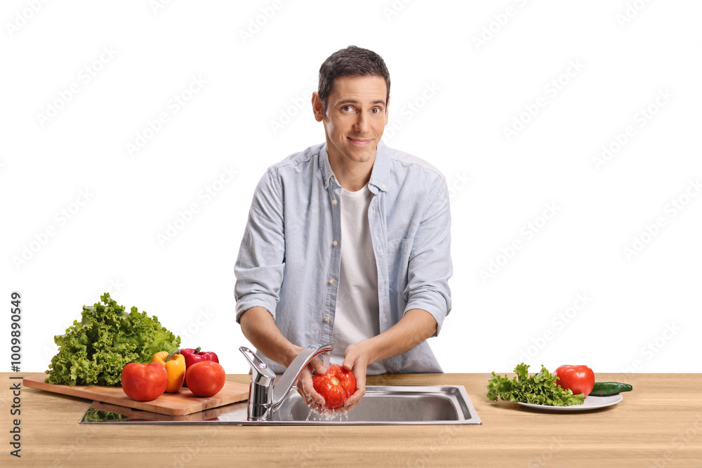 Young man washing tomato in a kitchen sink and smiling Young man washing tomato in a kitchen sink and smiling