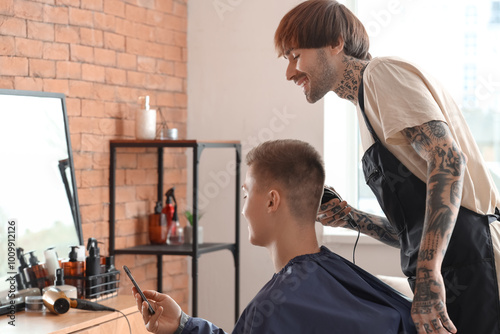 Male client with mobile phone showing hairstyle example to hairdresser in barbershop