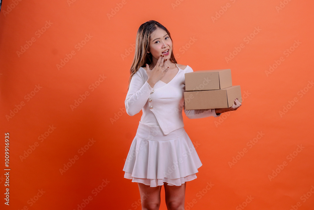 expression of indonesia woman in white top shocked to camera hand carrying 2 plain cardboard boxes while covering mouth, standing on orange background. for delivery, gift, expedition, service, package expression of indonesia woman in white top shocked to camera hand carrying 2 plain cardboard boxes while covering mouth, standing on orange background. for delivery, gift, expedition, service, package