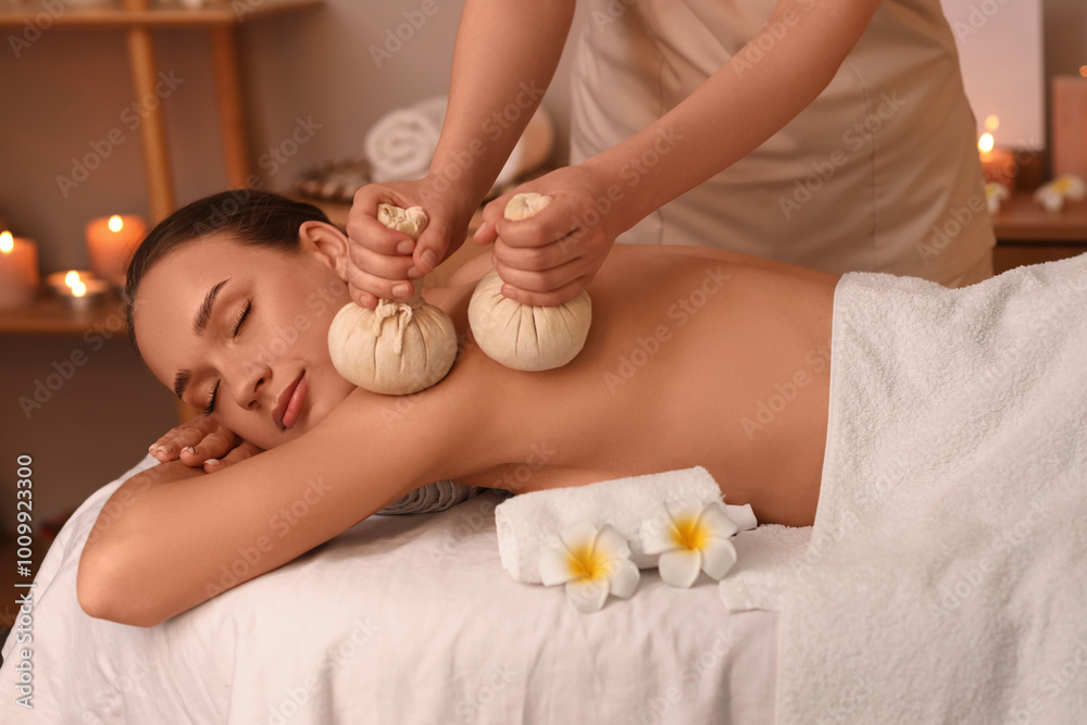 Young woman getting massage with herbal bags in dark spa salon Young woman getting massage with herbal bags in dark spa salon