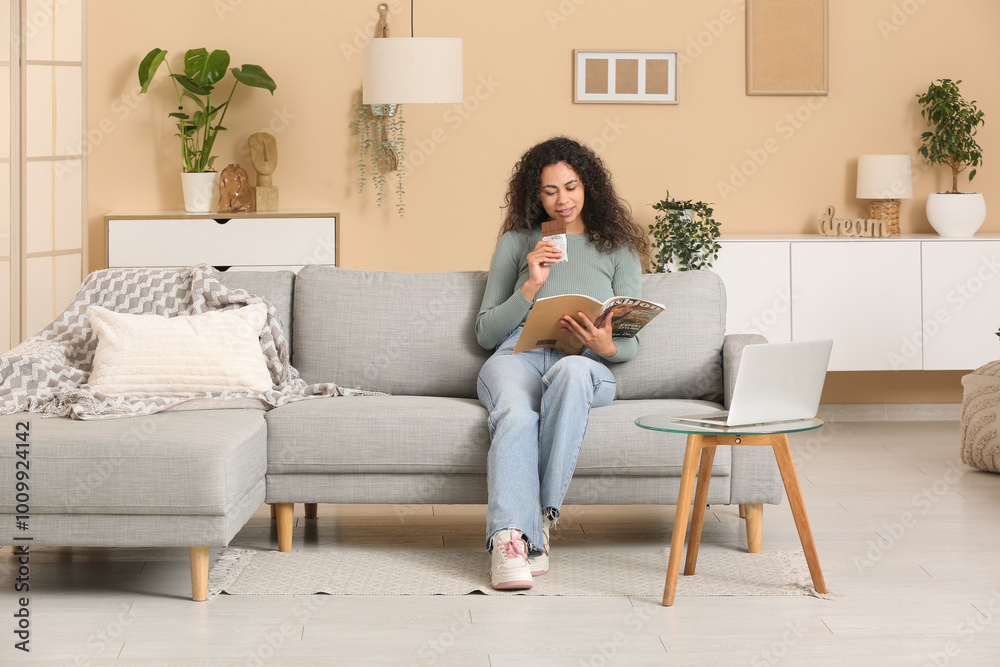 Young African-American woman eating chocolate and reading magazine at home Young African-American woman eating chocolate and reading magazine at home
