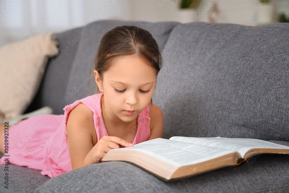Cute little girl reading Bible on sofa at home Cute little girl reading Bible on sofa at home