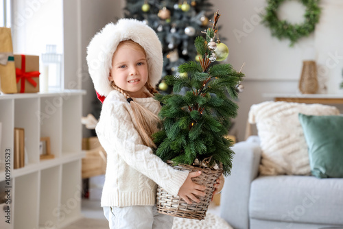 Cute little girl in Santa hat with Christmas tree at home