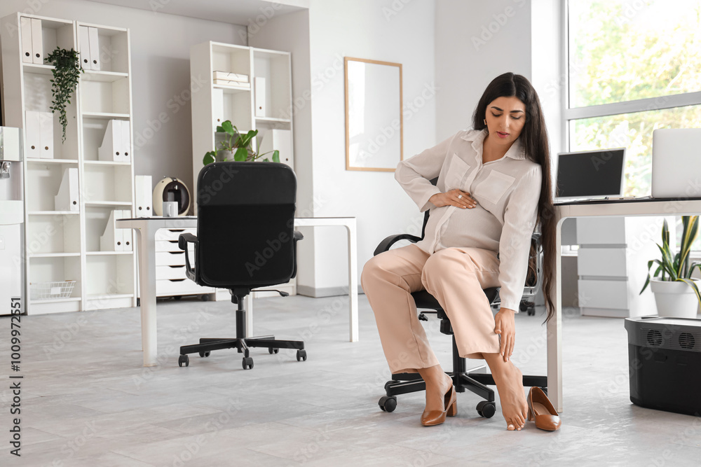 Fototapeta premium Pregnant businesswoman taking off her heels in office