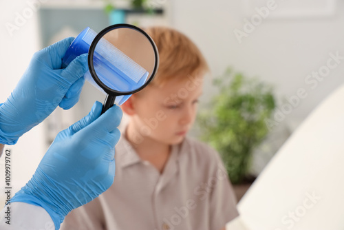 Female doctor with head lice comb and magnifier against little boy in clinic, closeup
