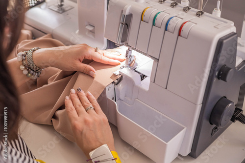 A plus size woman fashion designer uses an overlock sewing machine in her studio. A seamstress sews