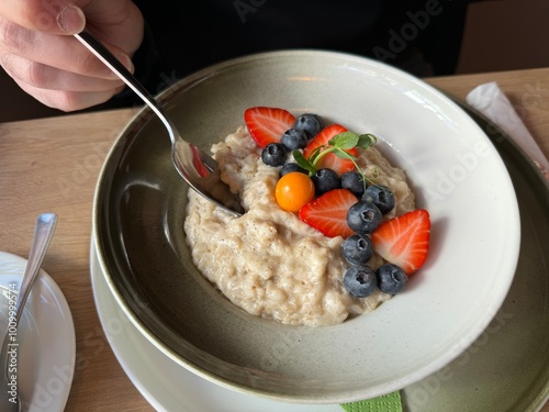 Koseverden & Koselig Cafe, Storgata, Tromsø, Norway - man dipping spoon in tasty breakfast oatmeal served with fresh berries strawberries, blueberries physalis photo