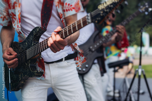 Concert view of electric guitar player with vocalist and rock band performing on open air arena, male musician guitarist on stage with audience in a crowded festival, hands on a guitar