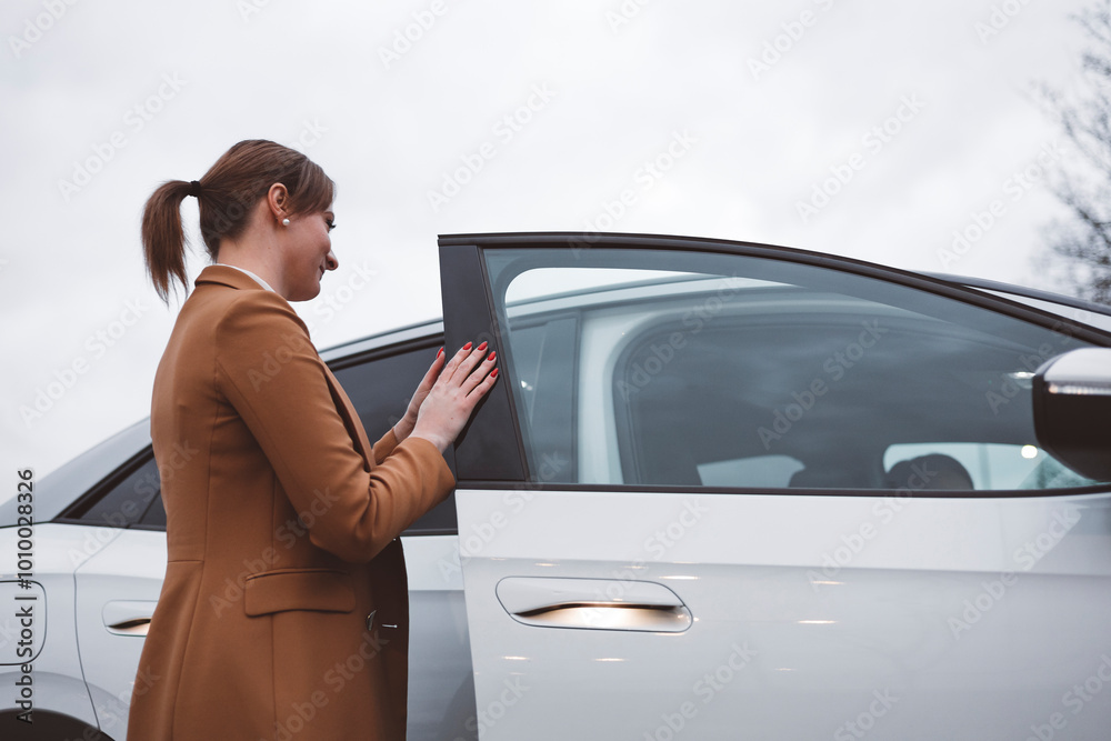 Naklejka premium Businesswoman waiting on the sidewalk to be picked up by an electric car driver