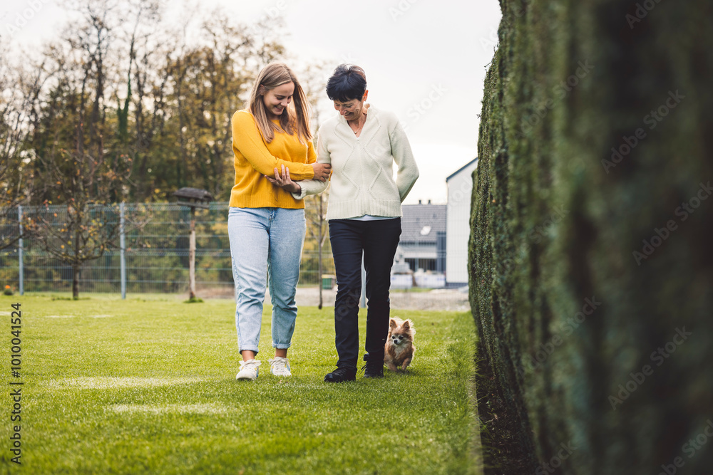 Fototapeta premium Walking together, coming from store, putting on jackets, carrying bags. Granddaughter helping her grandma walking at garden to keep her physical active.