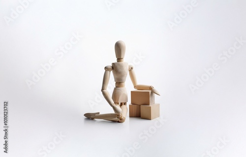 A wooden mannequin sits with its arm resting on a stack of three wooden blocks. photo