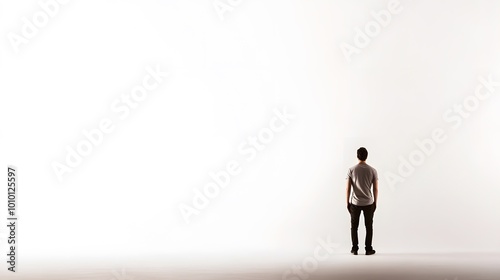 A young man stands in front of a white wall.