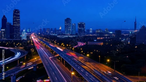 Timelapse with day changing to night. A nighttime cityscape with car lights creating light trails along a busy highway.