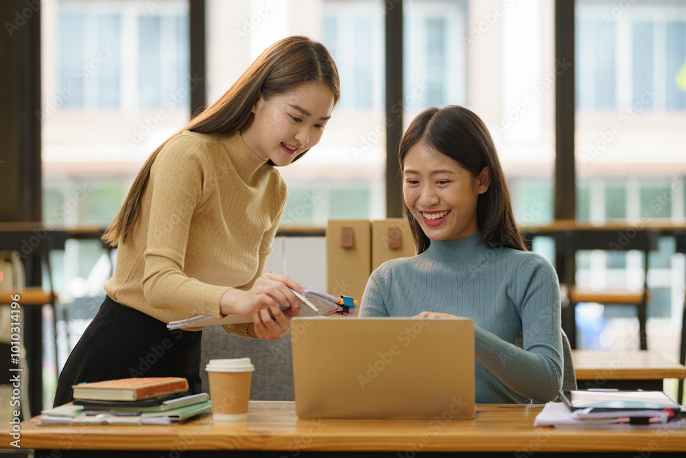 Two young Asian businesswomen discussed investment project work and planning strategy. Business people talk together on laptop computers at the office. Two young Asian businesswomen discussed investment project work and planning strategy. Business people talk together on laptop computers at the office.