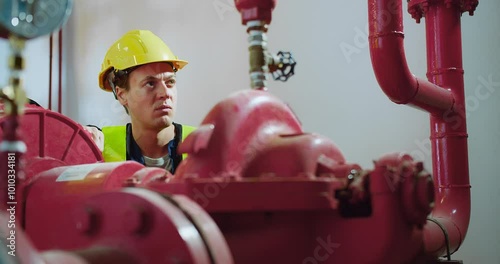 A worker in a yellow helmet and vest adjusts a pipe valve in an industrial setting, highlighting maintenance and safety within engineering environments, showcasing modern engineering practices.