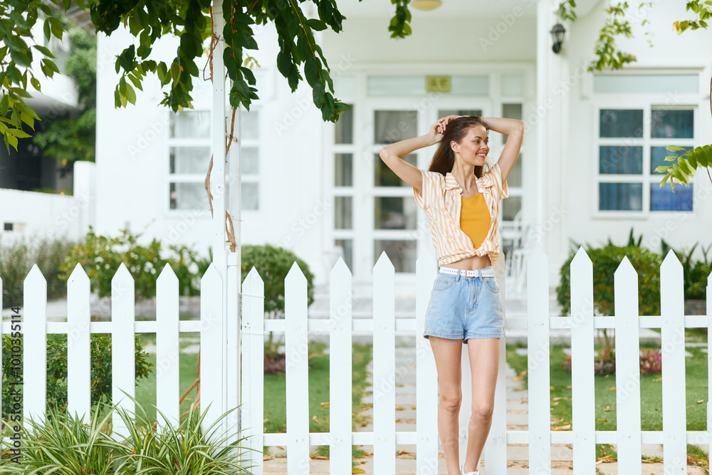 Φωτογραφία Young woman enjoying a sunny day by a white picket fence in front of a bright ho