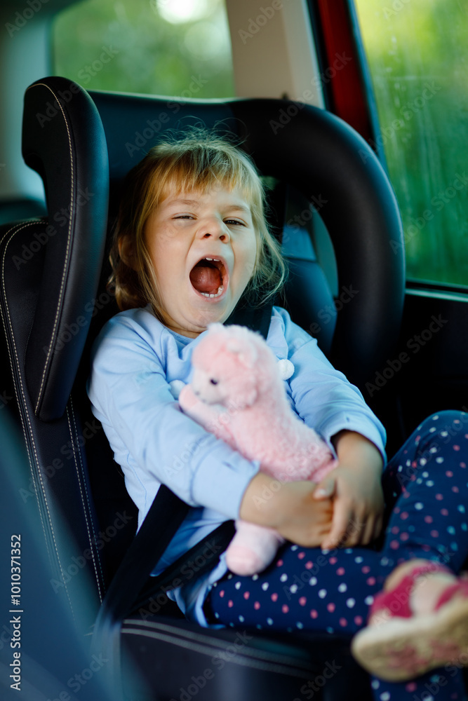 Φωτογραφία Adorable toddler girl sitting in car seat, holding plush soft toy and looking out of the window on nature and traffic