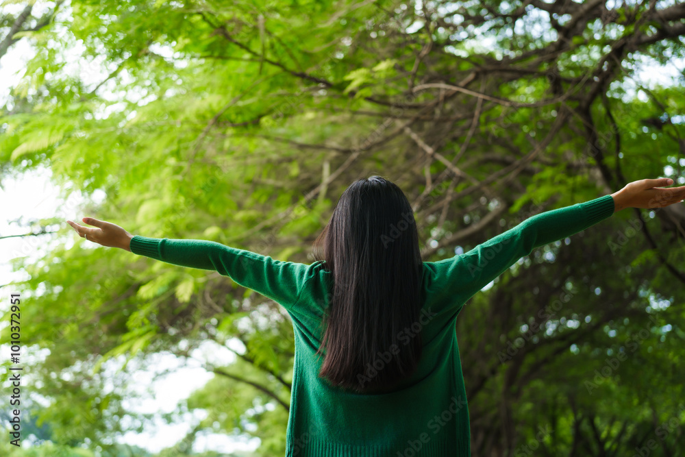 An Asian woman is standing happily in a green forest park, enjoying the fresh air and nature. She takes a deep breath, looks up at the morning sunlight, and feels relaxed and peaceful. An Asian woman is standing happily in a green forest park, enjoying the fresh air and nature. She takes a deep breath, looks up at the morning sunlight, and feels relaxed and peaceful.