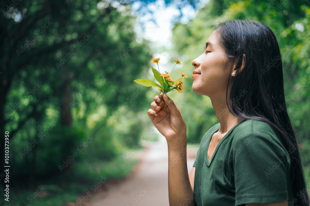 An Asian woman is happily relaxing in a green forest garden, smelling flowers and enjoying the fresh air. She takes a deep breath, looks up at the morning sunlight, and feels at peace with nature An Asian woman is happily relaxing in a green forest garden, smelling flowers and enjoying the fresh air. She takes a deep breath, looks up at the morning sunlight, and feels at peace with nature