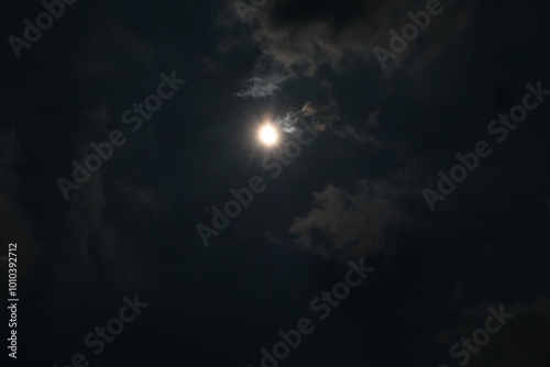 Hybrid Solar Eclipse. The night sky is filled with dark clouds, illuminated by the bright full moon and its magical moonlight.