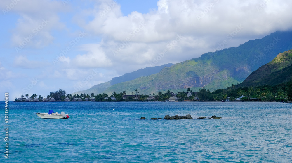 Scenic view of solo boat in turquoise ocean water of lagoon with over water beach huts and mountains on tropical island on Mo'orea, Tahiti in French Polynesia, South Pacific Scenic view of solo boat in turquoise ocean water of lagoon with over water beach huts and mountains on tropical island on Mo'orea, Tahiti in French Polynesia, South Pacific