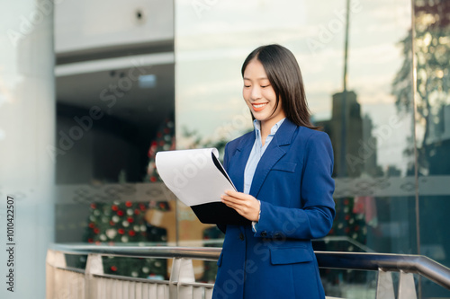 Asian woman with a smile standing holding notepad and tablet at out side office. big city on business center