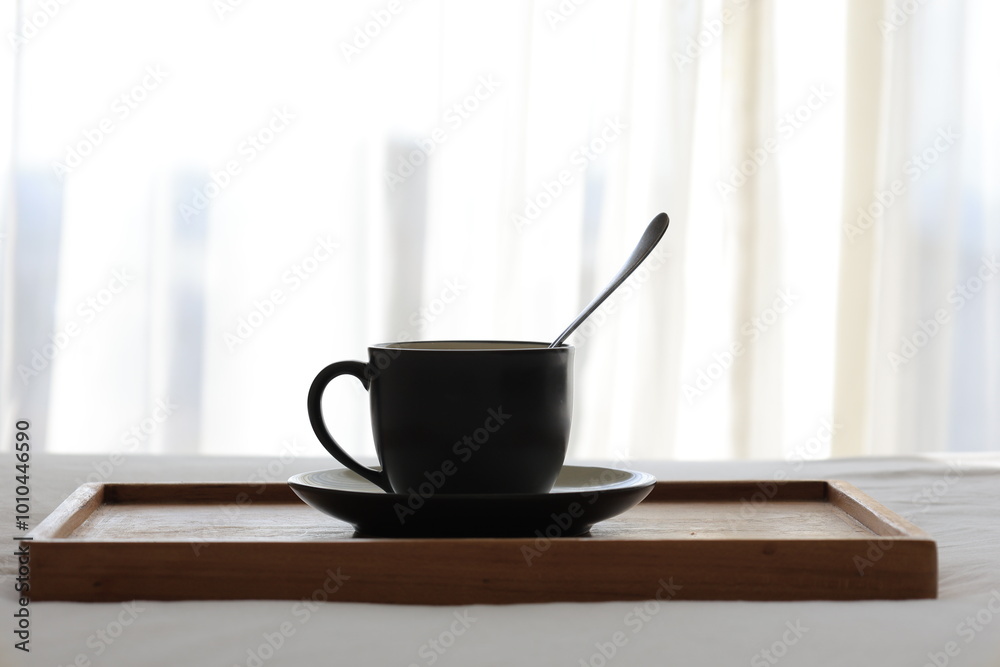 Obraz premium A black mug filled with steaming coffee sits on a wooden table, illuminated by the sun streaming in through a nearby window.