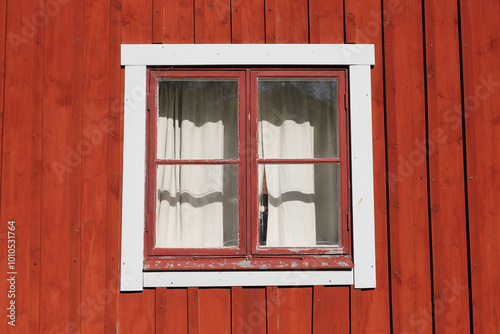 A red  wooden wall with an old window with curtain.