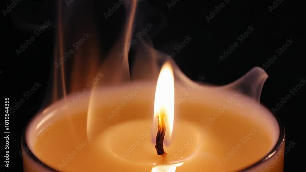 A single candle burns softly in the darkness, its flickering flame ...