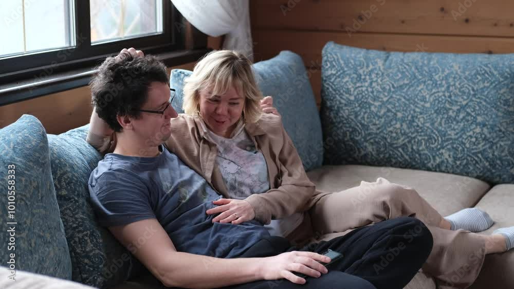 A man and a woman are relaxing on a sofa in the living room of their home. The family is having a nice time in the evening, relaxing after a working day. A man and a woman are relaxing on a sofa in the living room of their home. The family is having a nice time in the evening, relaxing after a working day.
