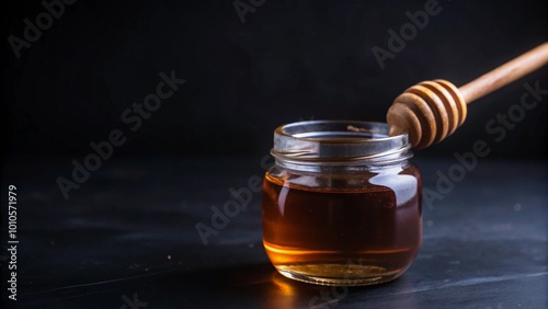 Close-up of a glass jar filled with golden honey, a wooden honey dipper resting on the rim, against a dark background. photo