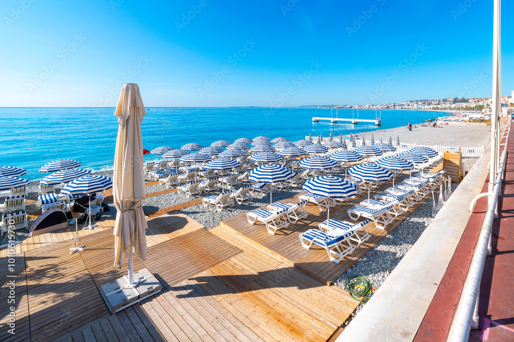 Φωτογραφία Turquoise sea, blue and white umbrellas, lounge chairs, and the pebble beach along the paved Promenade des Anglais and Bay of Angels, at the Cote d'Azur French Riviera, in Nice, France