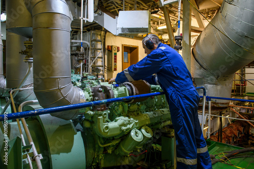 Marine Engineer in blue overall working in Engine room of ship. Work at sea. Motorman. photo