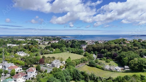 Guernsey high drone flight from upper fields towards La Charrotterie with views over St Peter Port Harbour and cruise liner at anchor on bright sunny day photo