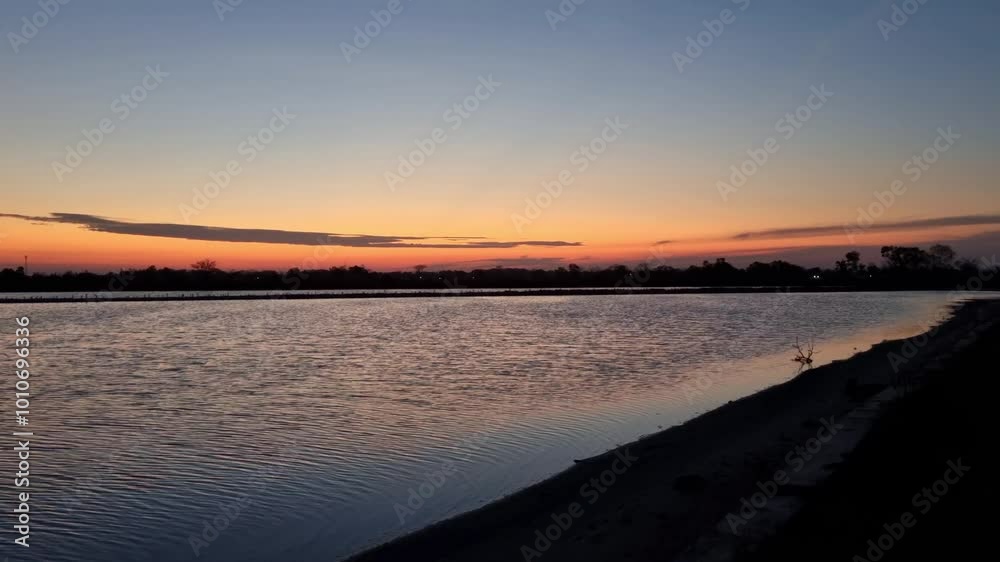 A beautiful sunset over a calm lake reflects orange and purple hues, captured in a serene landscape