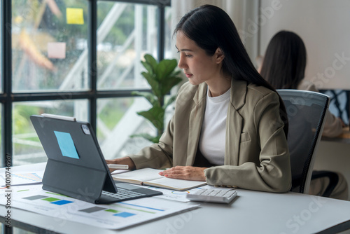 Businesswoman working on digital tablet and taking notes in modern office
