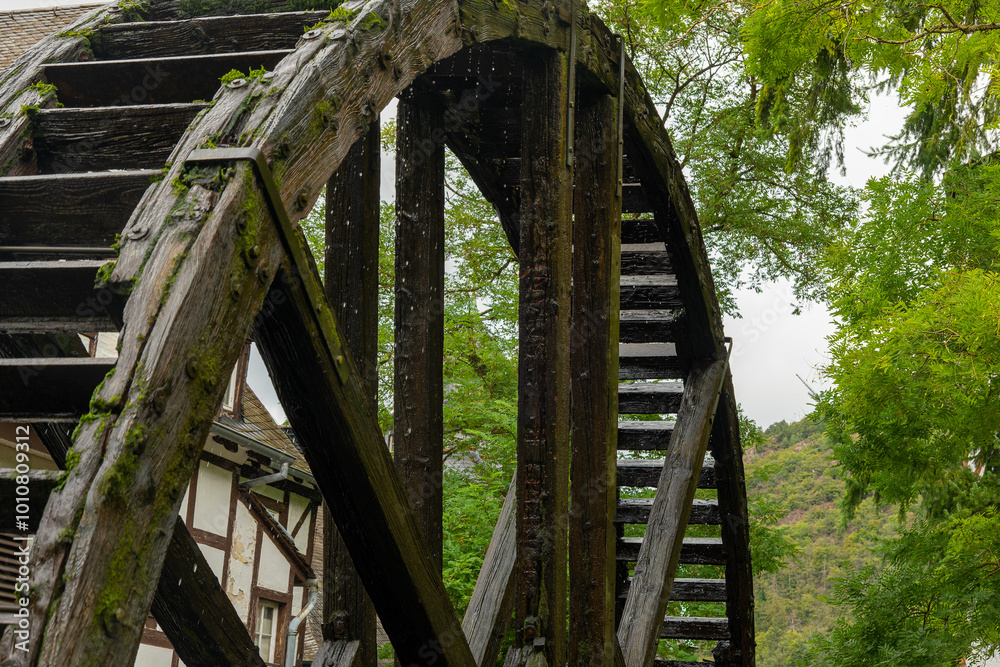 wooden water wheel with moss growing on it. The water wheel is surrounded by trees and a house wooden water wheel with moss growing on it. The water wheel is surrounded by trees and a house
