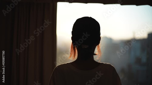 窓から夕日を見る女性の後ろ姿