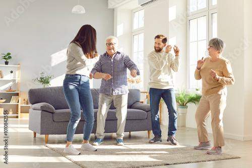 Happy joyful senior parents having fun with their adult children man and woman dancing in the living room at home enjoying time together. Family relationships and generations concept