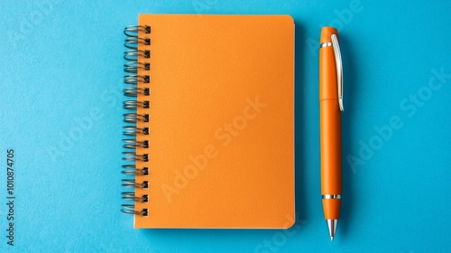 A plain orange pen sits on a blue background with a spiral notebook in the center. The notebook has no lines and is open.