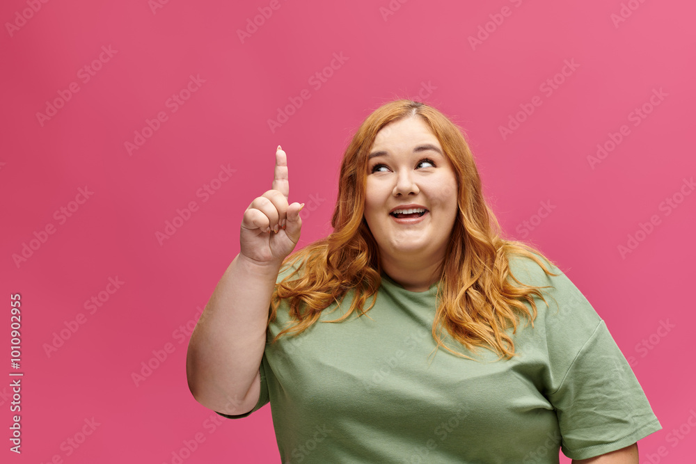 A plus size woman in a green shirt points upward with a thoughtful expression on her face. A plus size woman in a green shirt points upward with a thoughtful expression on her face.