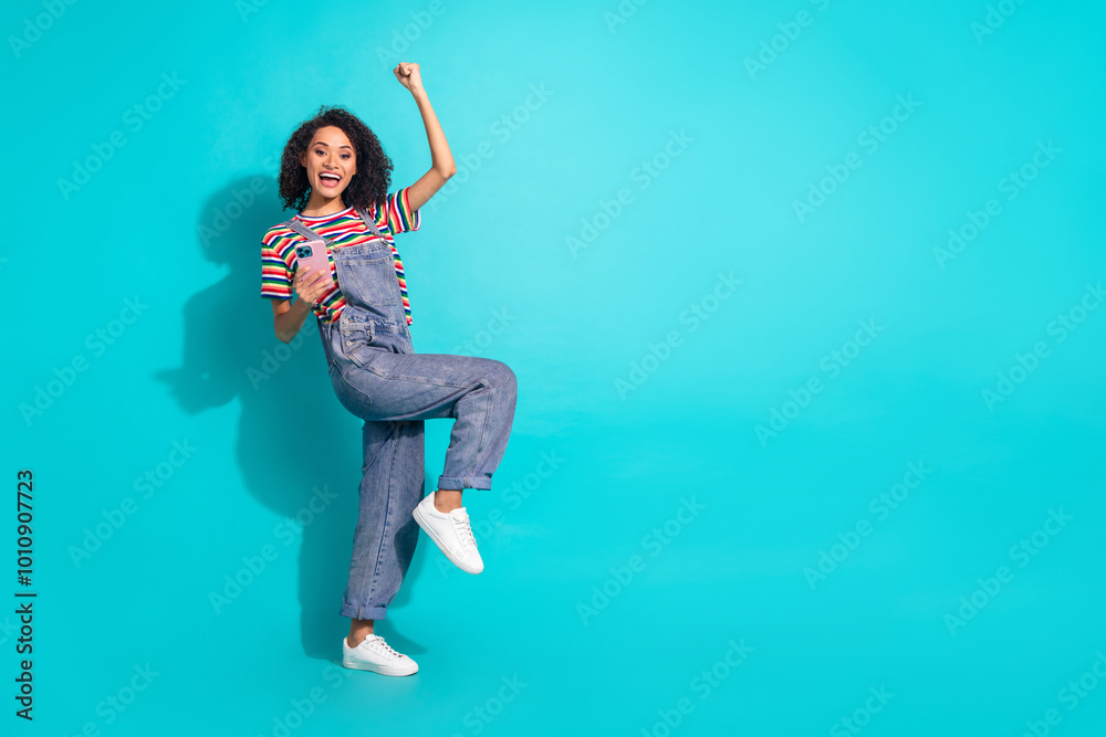 Φωτογραφία Photo of positive excited girl raise fists up use phone isolated cyan color back