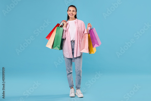 Smiling woman with colorful shopping bags on light blue background