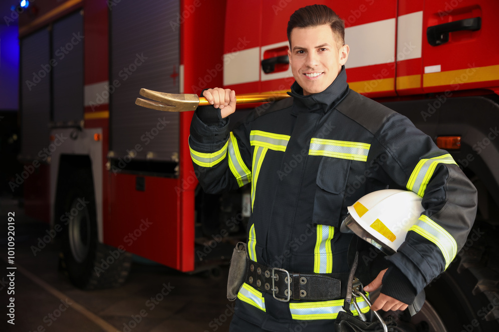 Fototapeta premium Portrait of firefighter in uniform with helmet and entry tool near fire truck at station, space for text