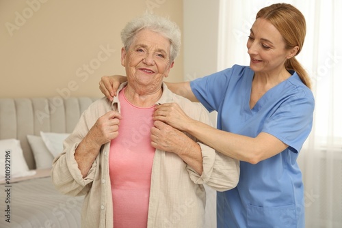 Healthcare worker helping senior woman to put on jacket at home