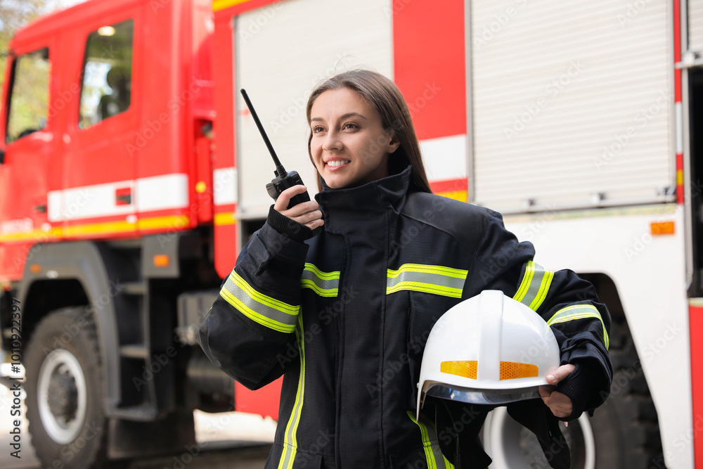 Firefighter in uniform using portable radio set near fire truck outdoors Firefighter in uniform using portable radio set near fire truck outdoors