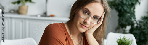 A woman with glasses and a gentle smile sits in a sunlit room.