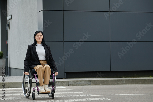 A woman in a wheelchair crosses a city street. photo