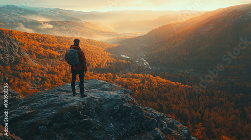 Hiker standing on mountain cliff overlooking autumn valley at sunrise 