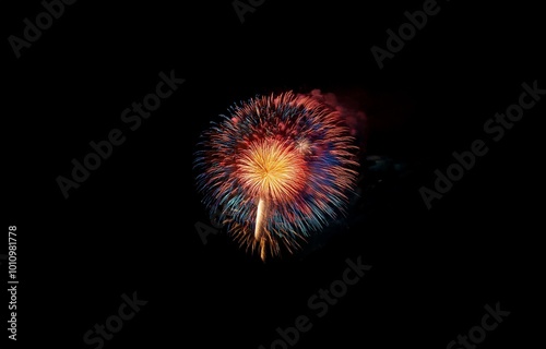 A colorful firework display with red, orange, and blue streaks explodes against a black night sky.